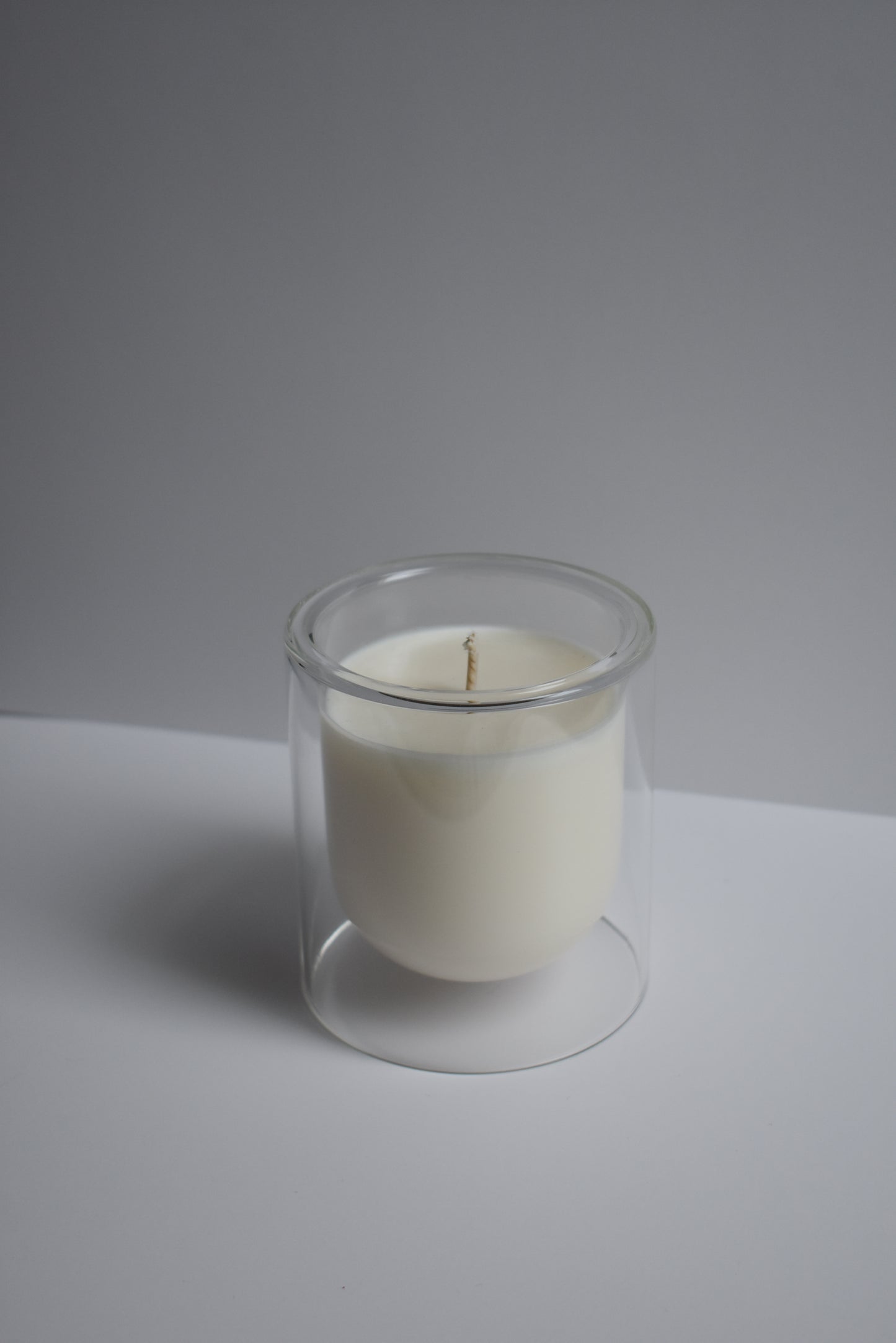 Clear candle holder with a white candle on a light gray background