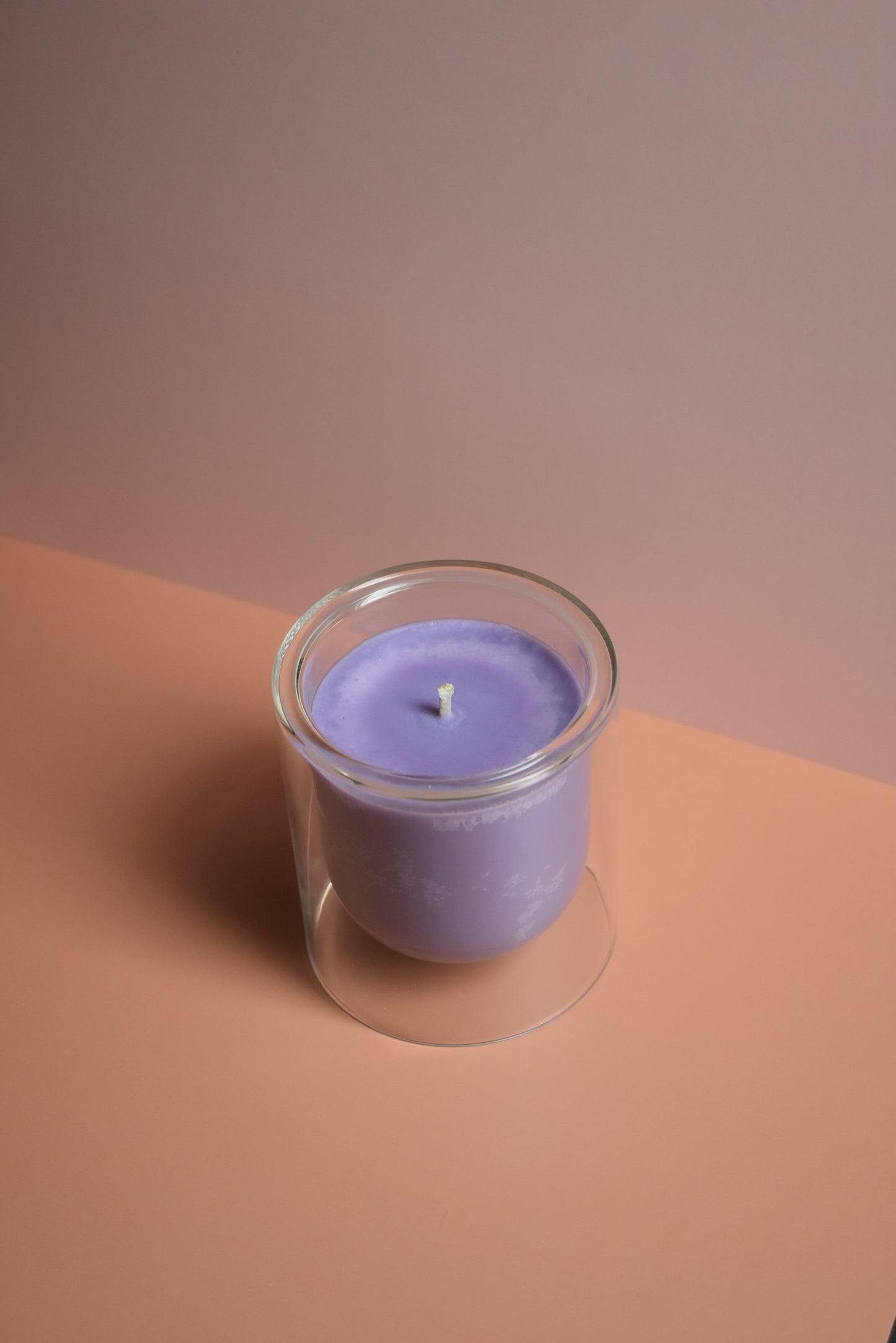 Purple candle in a clear glass holder on a two-tone brown background
