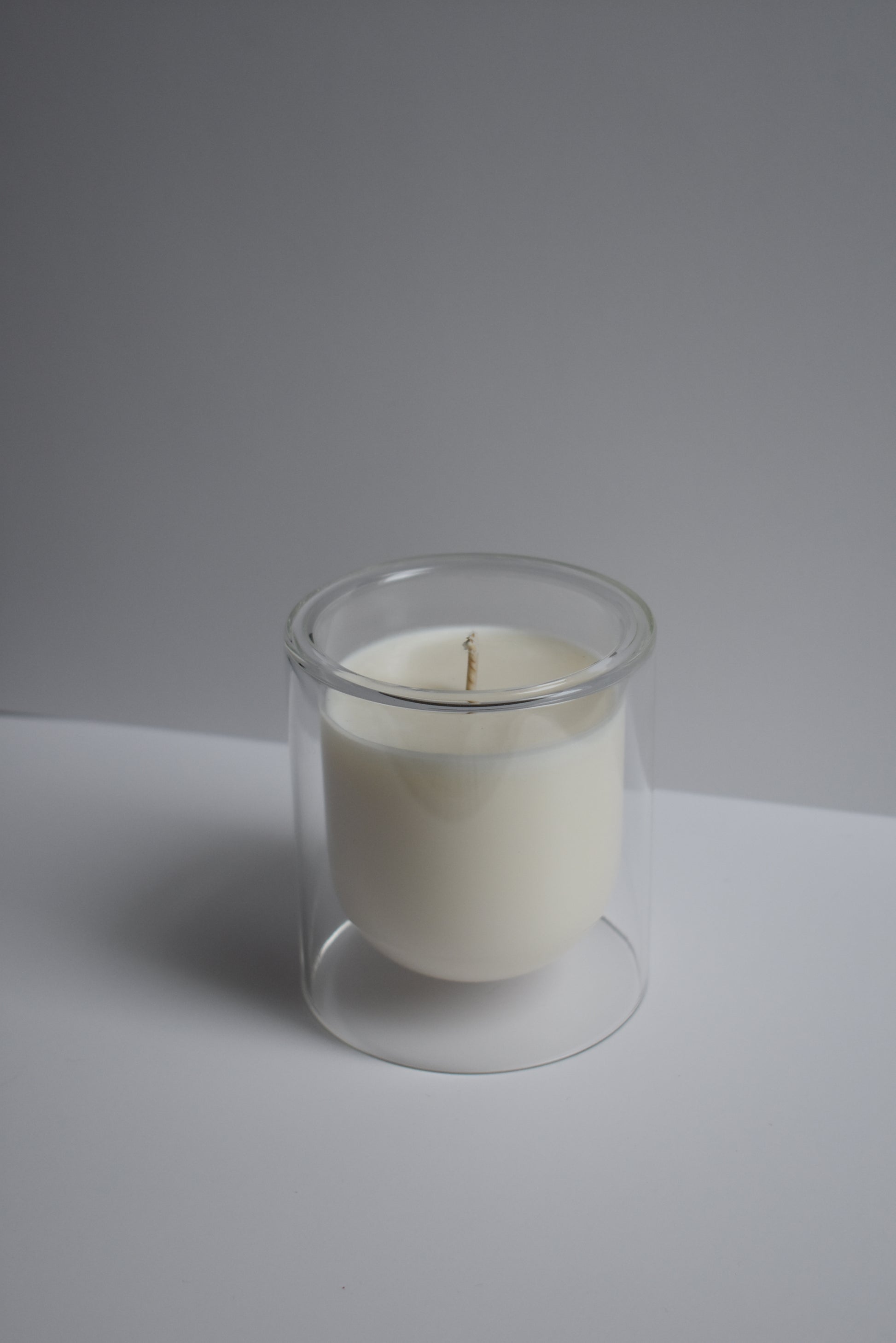Clear candle holder with a white candle on a light gray background