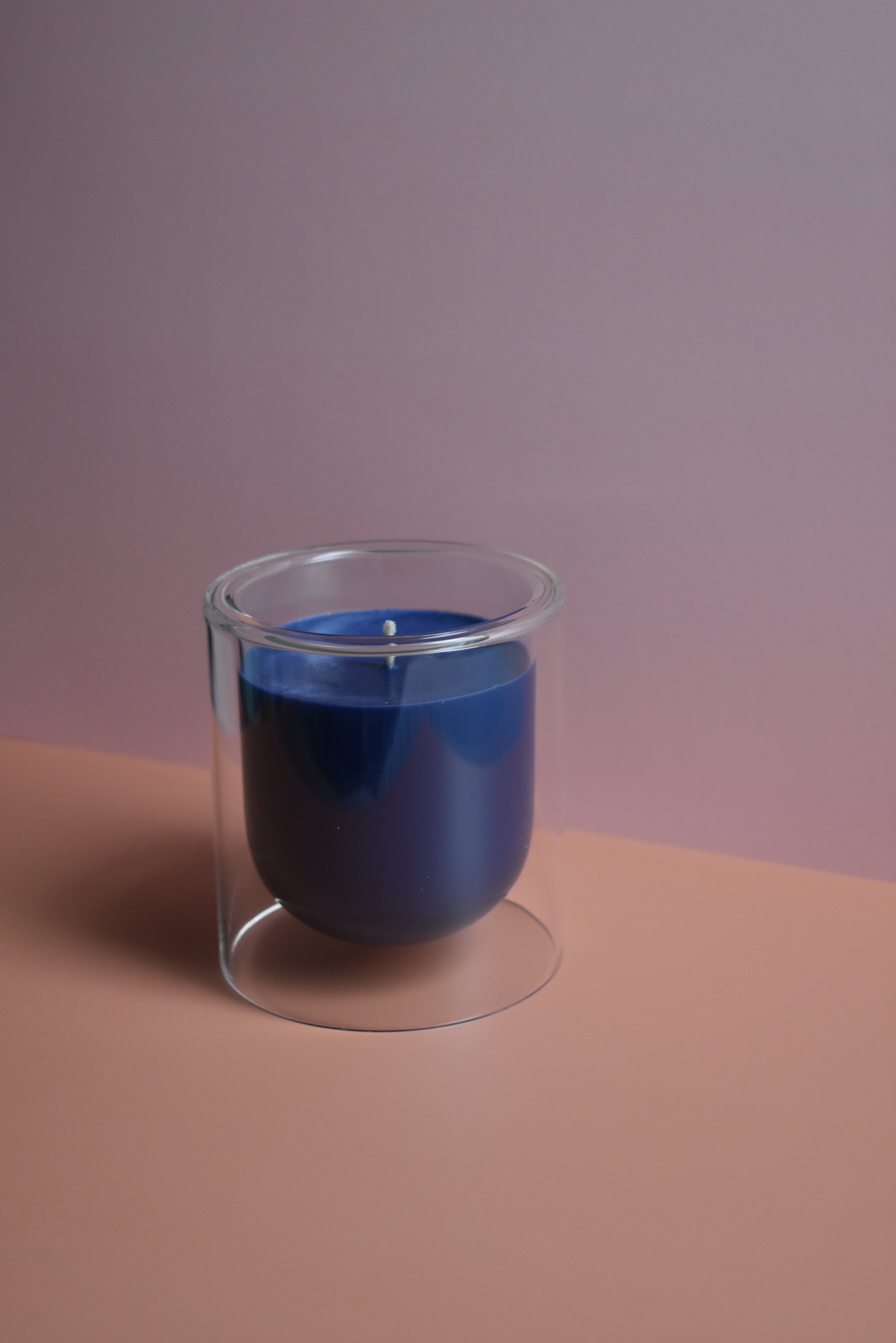 Clear glass container with blue candle on a two tone pink background
