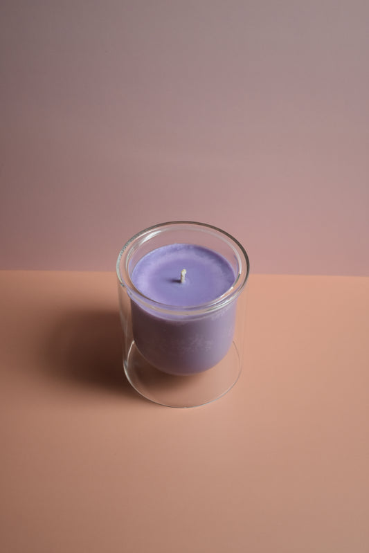 Purple candle in a clear glass holder on a two-tone brown background