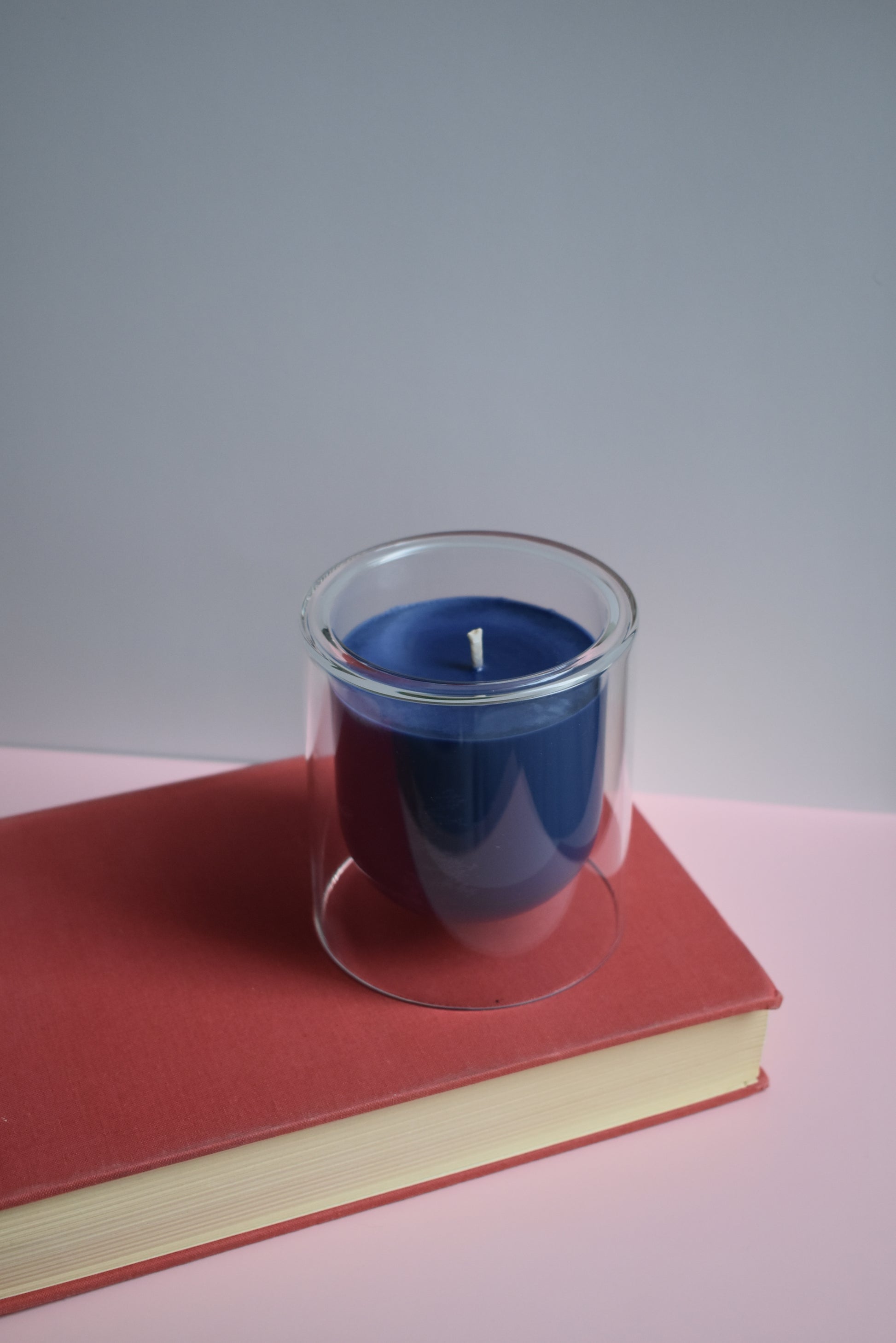 Blue candle in a glass holder on a red book with a white background